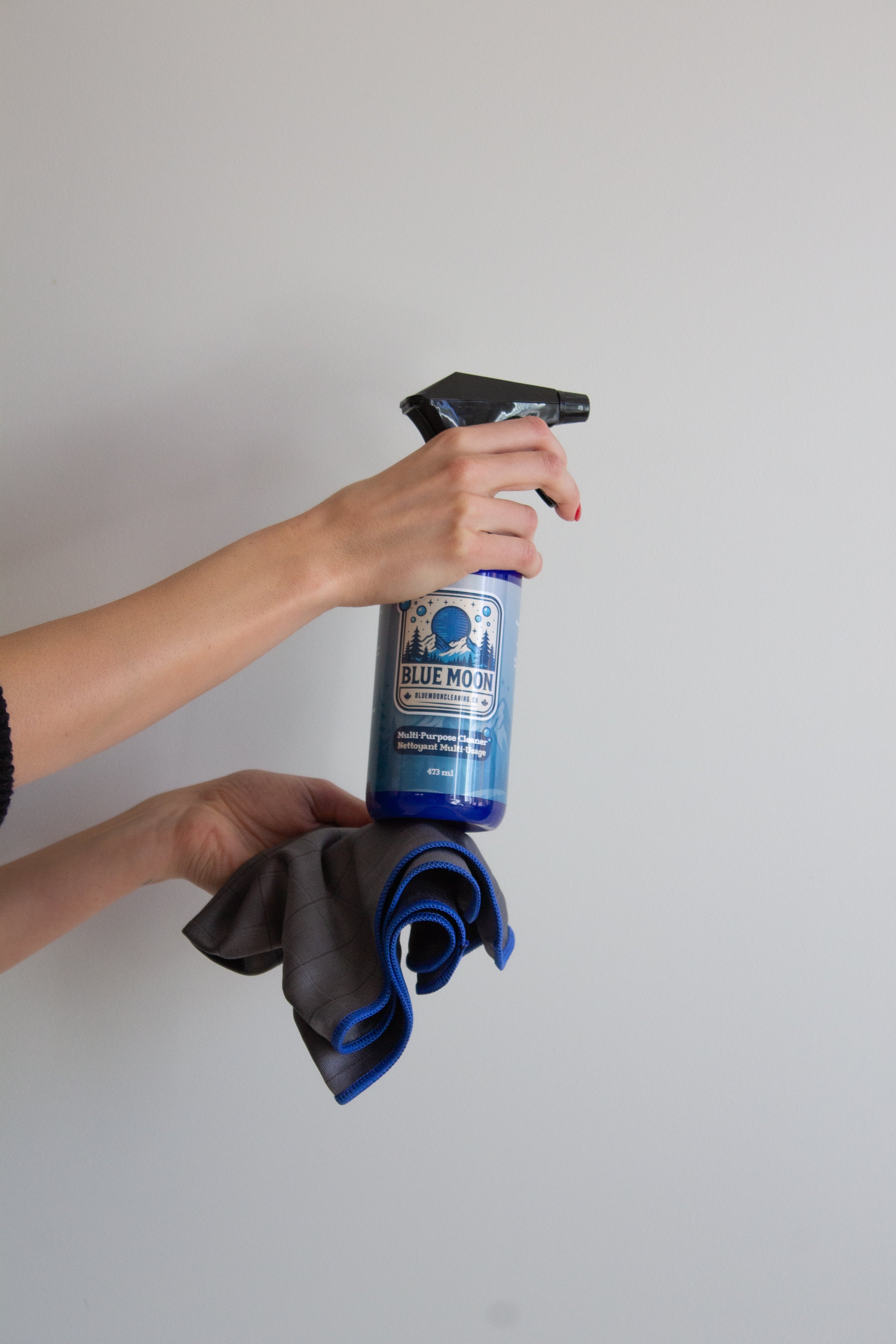 Person holding a spray bottle and microfiber cloths against a plain background